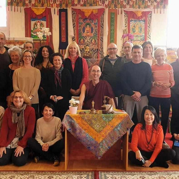 Groupe en méditation bouddhiste tibétaine avec lama, thangkas et objets rituels