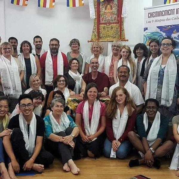 Groupe en méditation bouddhiste tibétaine avec écharpes blanches et drapeaux sacrés