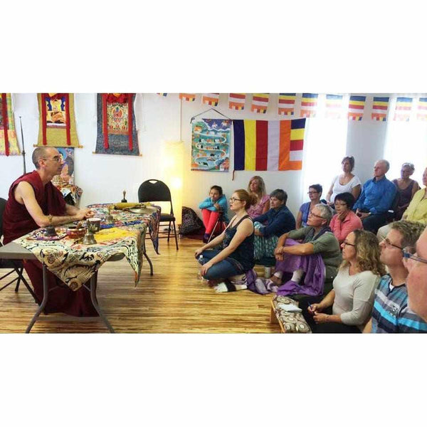 Lama enseignant la méditation bouddhiste tibétaine à un groupe, drapeaux et thangkas en arrière-plan