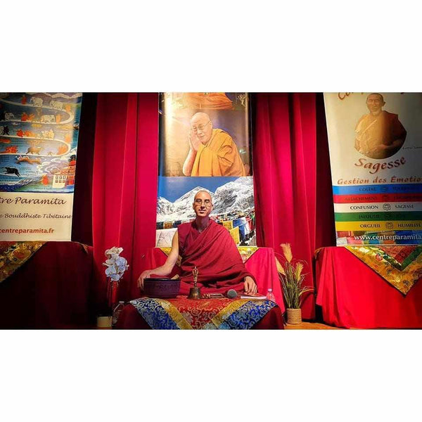 Lama Samten en robe rouge, enseignant la méditation bouddhiste tibétaine devant portrait du Dalaï Lama et bannières spirituelles