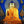 Statue de Bouddha dorée avec robe orange, coiffure bleue et auréole scintillante, objets tibétains autour