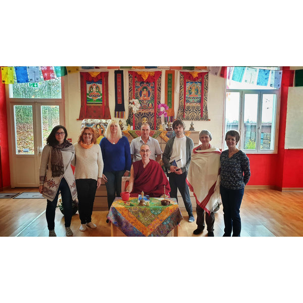 Groupe lors d'une conférence de méditation bouddhiste avec maître en robe rouge, thangkas et drapeaux tibétains