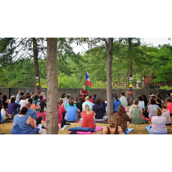 Conférence de méditation bouddhiste en plein air avec Lama Samten, drapeaux tibétains et public assis sur tapis.