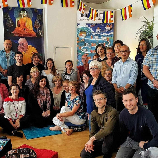 Groupe en méditation bouddhiste avec drapeaux tibétains et peinture du Bouddha