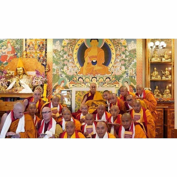Groupe de moines bouddhistes tibétains en robe orange devant thangka et statue de Bouddha