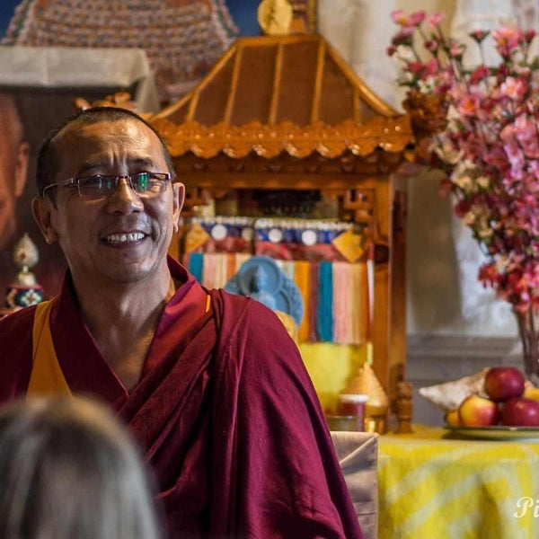 Lama bouddhiste souriant en robe rouge, enseignant la méditation dans un temple tibétain avec offrandes et fleurs