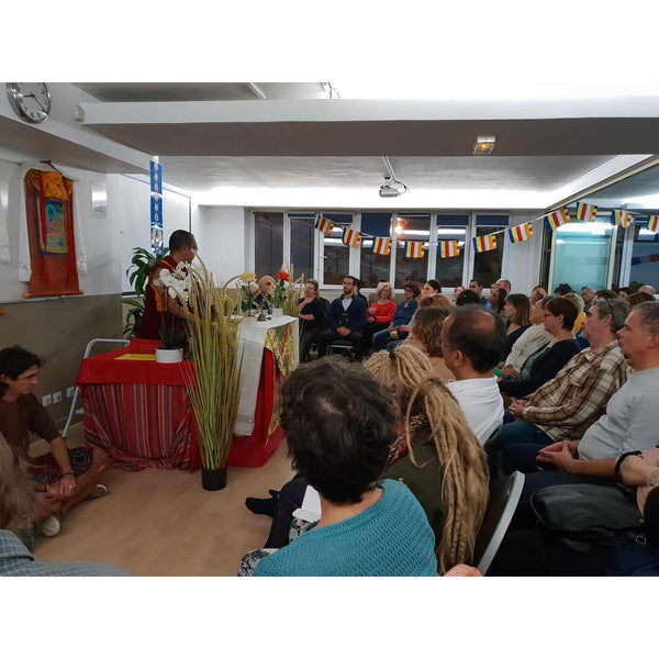 Conférence de méditation bouddhiste avec enseignant en robe safran, drapeaux tibétains et public attentif