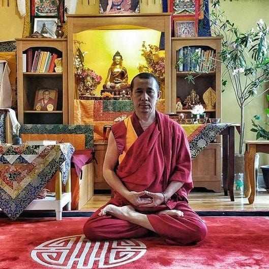 Moine bouddhiste en méditation devant autel tibétain avec statue de Bouddha et livres de philosophie