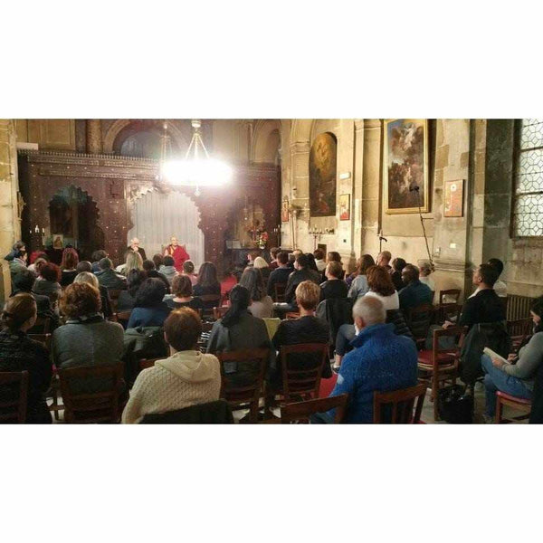 Conférence sur la méditation avec un maître bouddhiste devant un public attentif dans une salle ornée