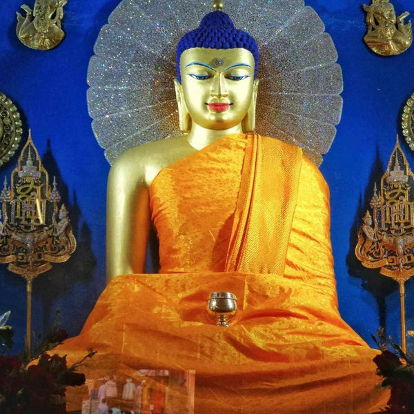 Statue de Bouddha dorée avec robe orange, halo scintillant, sur fond bleu, objets tibétains