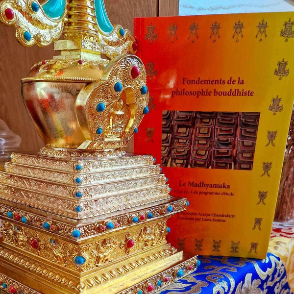 Stupa bouddhiste doré orné de pierres, à côté du livre 'Fondements de la philosophie bouddhiste'