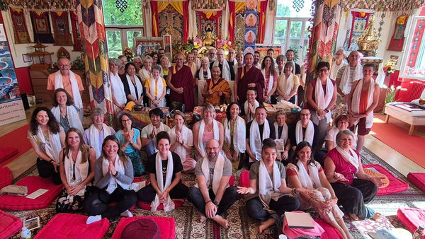 Groupe en méditation bouddhiste tibétaine avec lama, écharpes blanches, tapis rouges et drapeaux sacrés