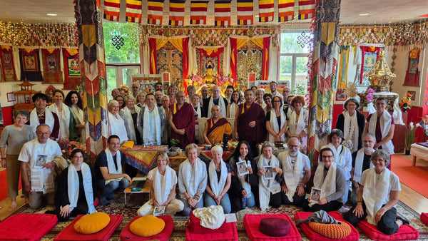 Groupe en méditation bouddhiste tibétaine avec lamas, drapeaux sacrés et offrandes, dans un centre spirituel