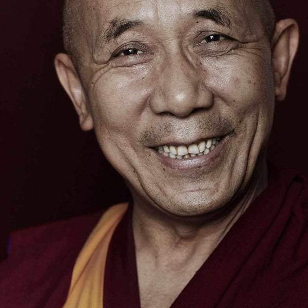 Moine bouddhiste souriant en robe rouge et or, symbole de sagesse et méditation tibétaine