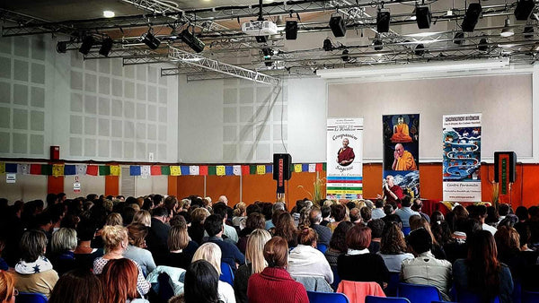 Conférence sur la méditation bouddhiste avec Lama Samten devant un public, drapeaux tibétains et affiches sur la sagesse et la compassion.