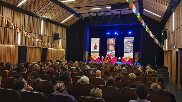 Conférence de méditation bouddhiste avec Lama Samten, drapeaux tibétains, public attentif dans salle en bois