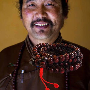 Lama bouddhiste souriant avec un mala en bois rouge, symbole de méditation et philosophie tibétaine