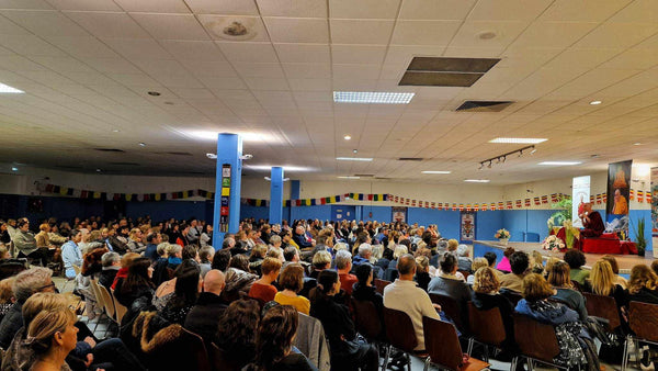 Conférence sur la méditation bouddhiste avec un maître tibétain devant un public attentif, drapeaux prières colorés.