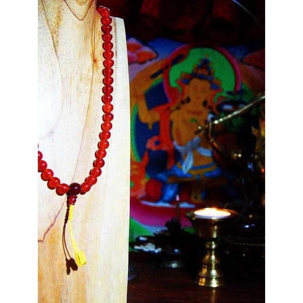 Chapelet bouddhiste en perles rouges avec tassel jaune, devant thangka et lampe à huile