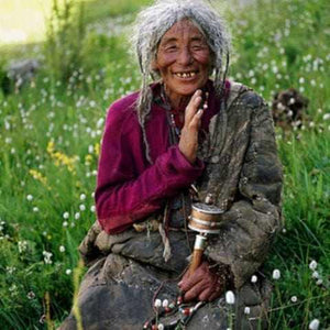 Femme tibétaine souriante avec moulin à prières dans un champ fleuri, culture bouddhiste himalayenne