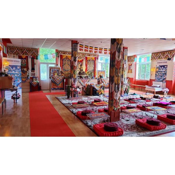 Salle de méditation bouddhiste avec coussins, tapis et drapeaux tibétains pour la pratique spirituelle.