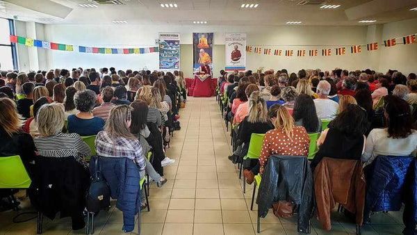 Conférence sur la méditation bouddhiste avec public assis, drapeaux tibétains et affiches philosophiques