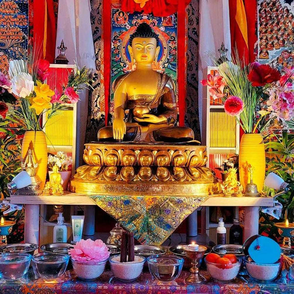 Statue dorée de Bouddha en méditation, autel tibétain avec offrandes, fleurs et thangkas, symboles bouddhistes