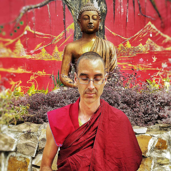 Moine bouddhiste en robe rouge méditant devant statue de Bouddha et mur peint, philosophie tibétaine