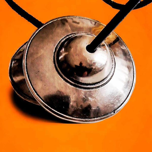 Cymbales tibétaines en métal pour méditation et rituels bouddhistes, fond orange vif