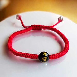 Bracelet rouge tibétain avec perle noire gravée de symboles bouddhistes, objet de méditation et protection spirituelle.