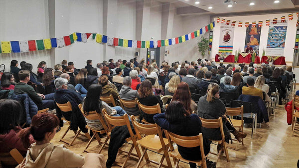 Conférence de méditation bouddhiste avec drapeaux tibétains et public attentif