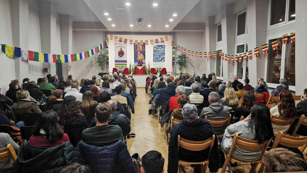 Auditoire lors d'une conférence sur la méditation bouddhiste avec drapeaux tibétains et affiches philosophiques