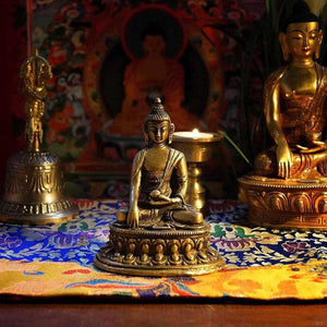 Statue de Bouddha en bronze sur tapis tibétain, avec cloche et thangka en arrière-plan