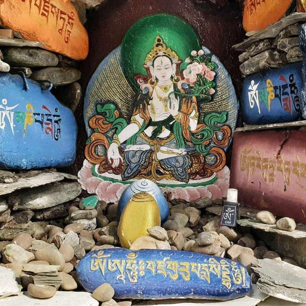 Statue bouddhiste tibétaine colorée avec pierres gravées, symboles de méditation et culture himalayenne