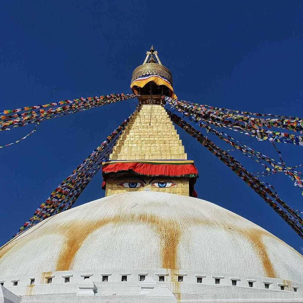 Stupa bouddhiste avec yeux de sagesse et drapeaux de prière colorés sous ciel bleu