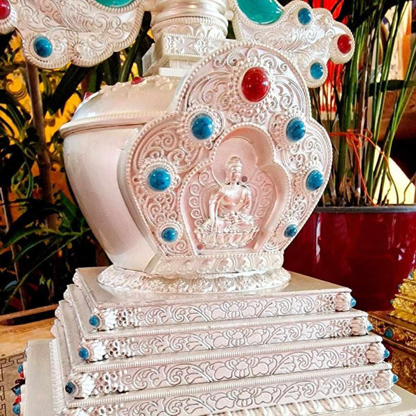 Stupa bouddhiste tibétain orné de pierres turquoise et rouges, avec statue de Bouddha, symbole de méditation et philosophie bouddhiste.