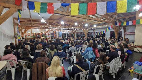 Conférence sur la méditation avec drapeaux tibétains, public assis dans salle en bois
