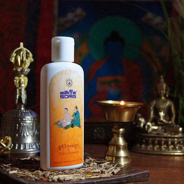 Huile tibétaine Zathi-Duknuum pour soins naturels, entourée d'objets bouddhistes et d'une lampe à huile