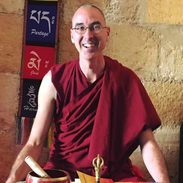 Lama Samten en robe bouddhiste rouge, souriant devant drapeaux tibétains et bol chantant