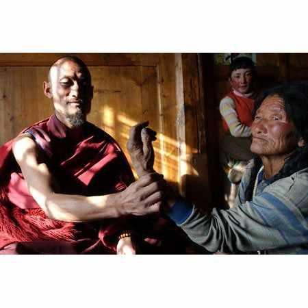 Lama bouddhiste en robe rouge bénissant une personne âgée dans un cadre tibétain traditionnel