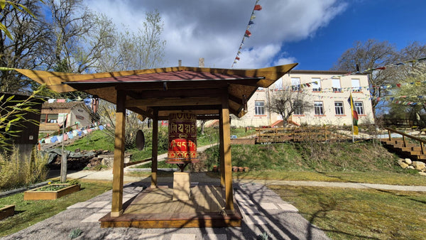 Roue de prière bouddhiste tibétaine sous kiosque en bois, drapeaux de prière, jardin paisible