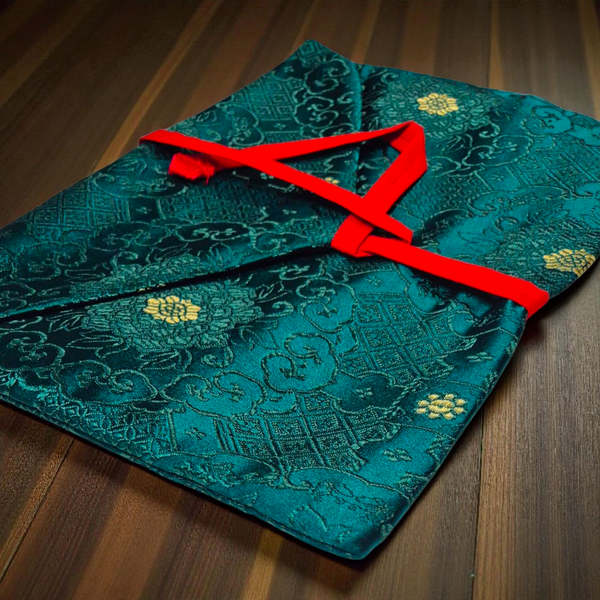 Pochette tibétaine en soie turquoise avec motifs dorés et ruban rouge, objet de philosophie bouddhiste