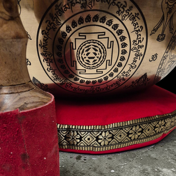 Gong tibétain gravé avec mandala et symboles bouddhistes, posé sur coussin rouge