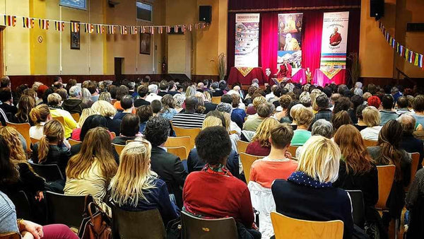 Conférence sur la méditation bouddhiste avec Lama Samten, public attentif dans salle décorée de drapeaux tibétains